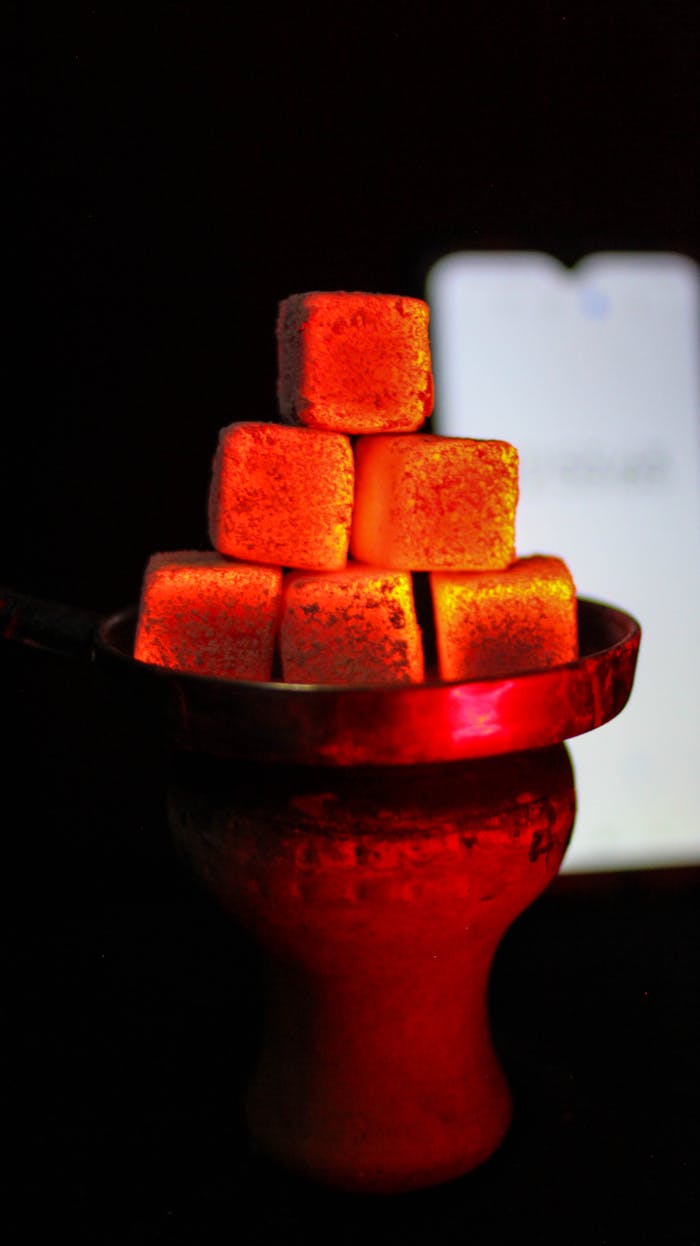 A close-up photo of glowing charcoal cubes stacked on a hookah bowl, emitting vibrant red heat.