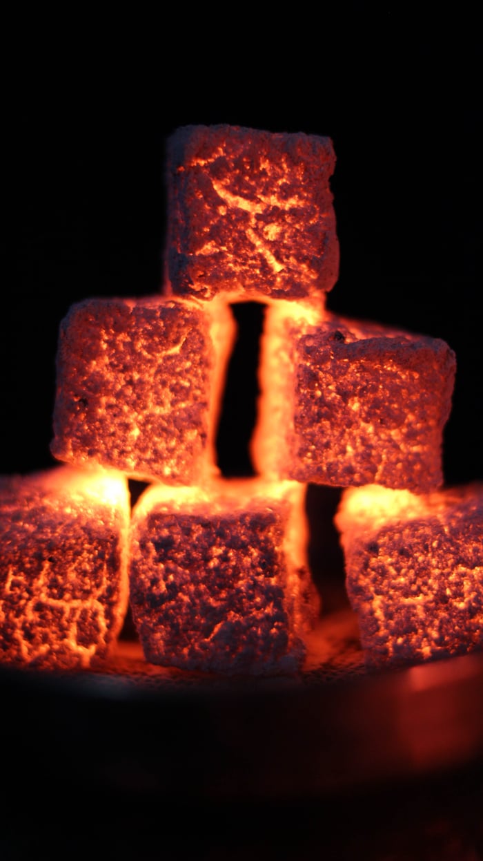 Close-up of glowing charcoal cubes stacked against a dark background, showcasing heat and texture.
